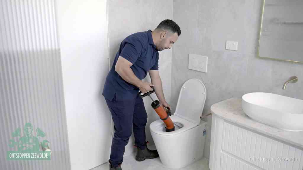 Een monteur buigt over een wandcloset en duwt met de hand een persluchtontstopper in de toiletpot om de verstopping handmatig los te maken in Zeewolde