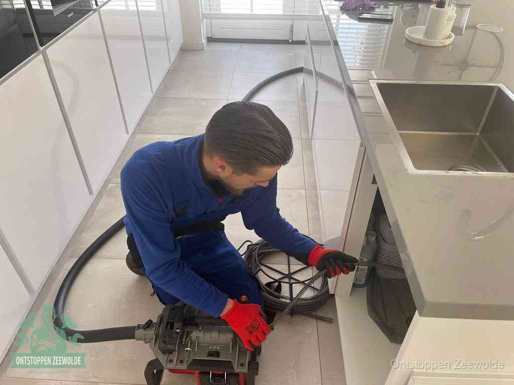 Een monteur ontstopt de keukenafvoer onder de spoelbak met een elektrische veermachine in Zeewolde