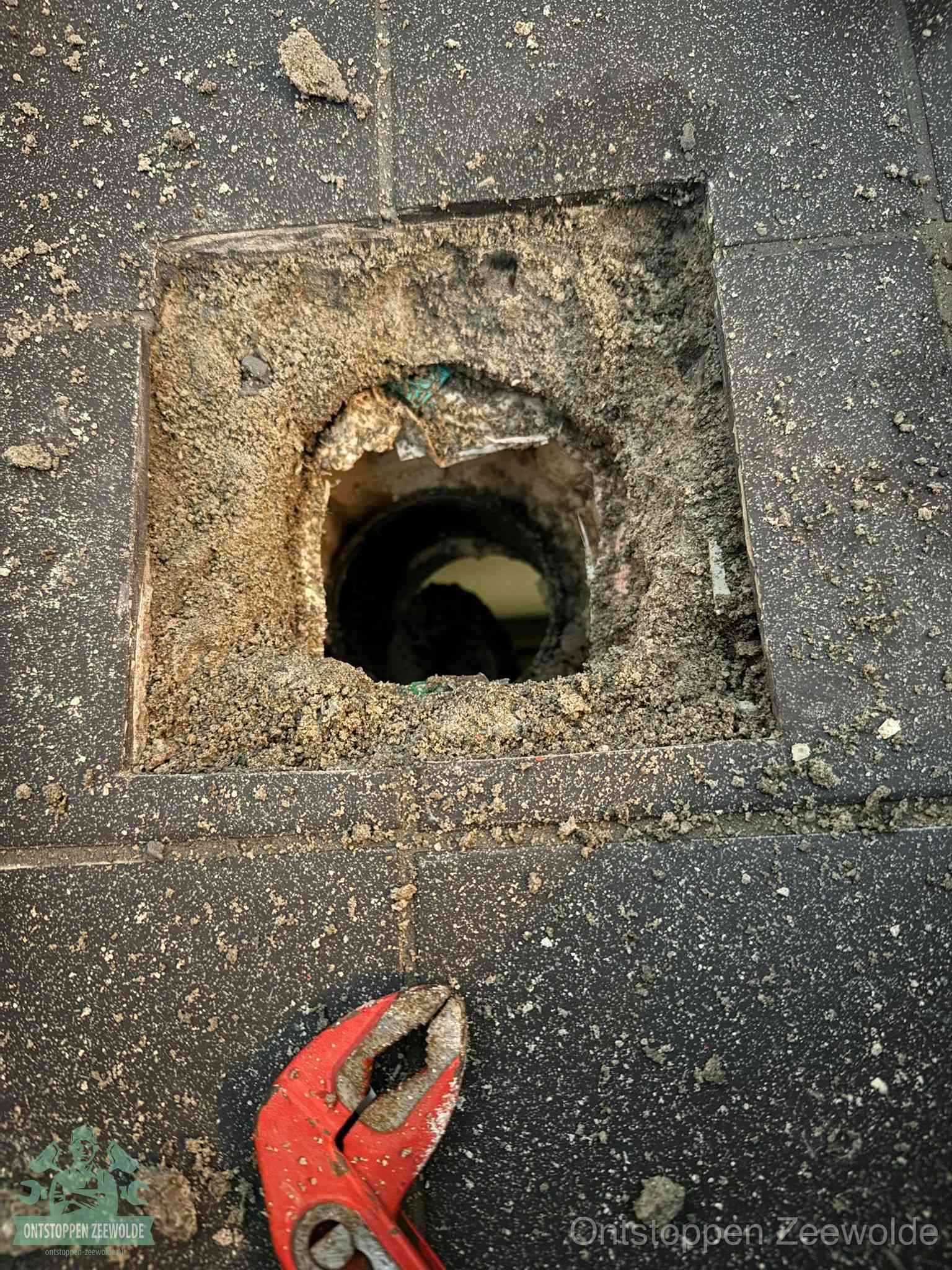 Een geopend rioolputje in een betontegelvloer met losgemaakt rooster en een zichtbare ronde afvoerbuis, het achterhalen waar de afvoerverstopping zit in Zeewolde