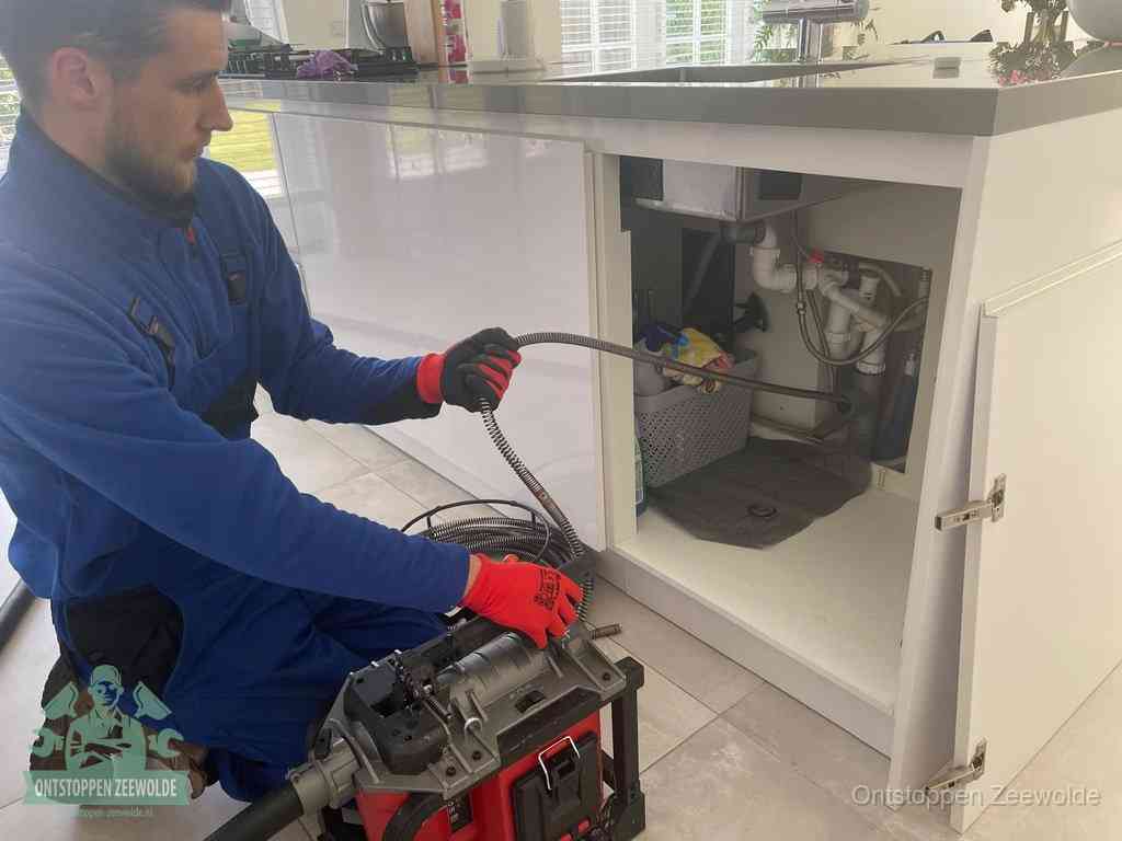 Monteur voert een ontstoppingsveer in de afvoer onder de keuken in Zeewolde