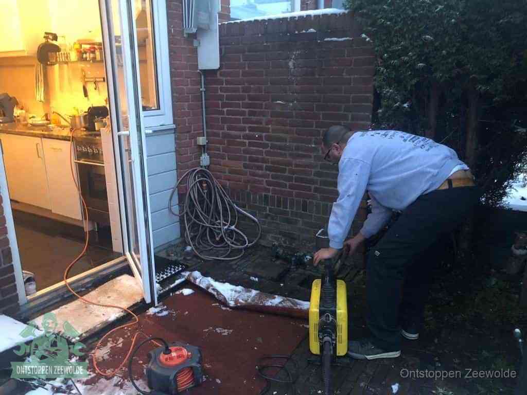 Een monteur werkt buiten bij een open riool-/grondput met een elektrische ontstoppingsmachine om een verborgen afvoerprobleem op te sporen in Zeewolde