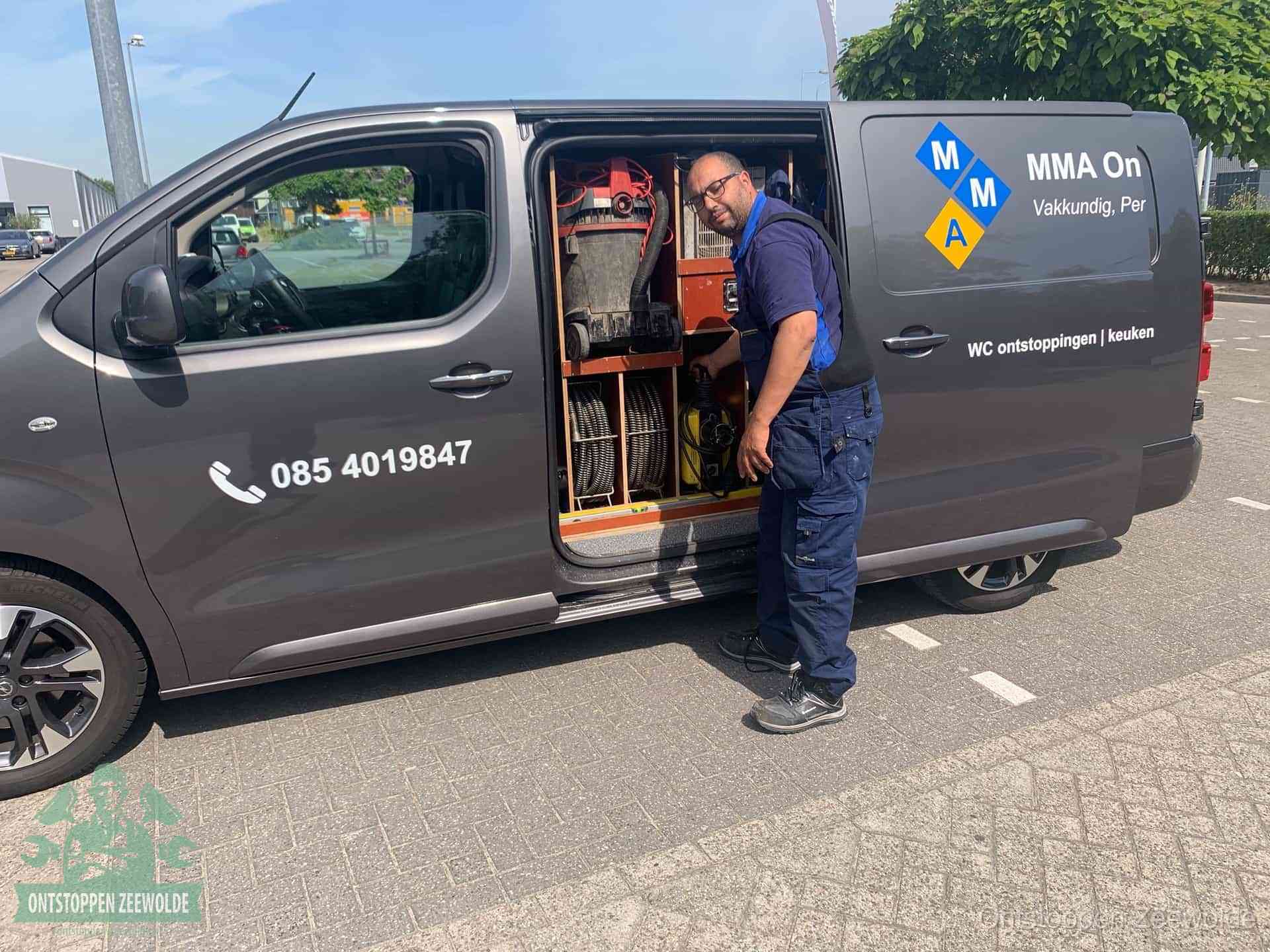 Een monteur bij de open schuifdeur van zijn bedrijfsbus op een parkeerplaats, klaar om de oorzaak van terugkerende afvoerverstoppingen aan te pakken in Zeewolde