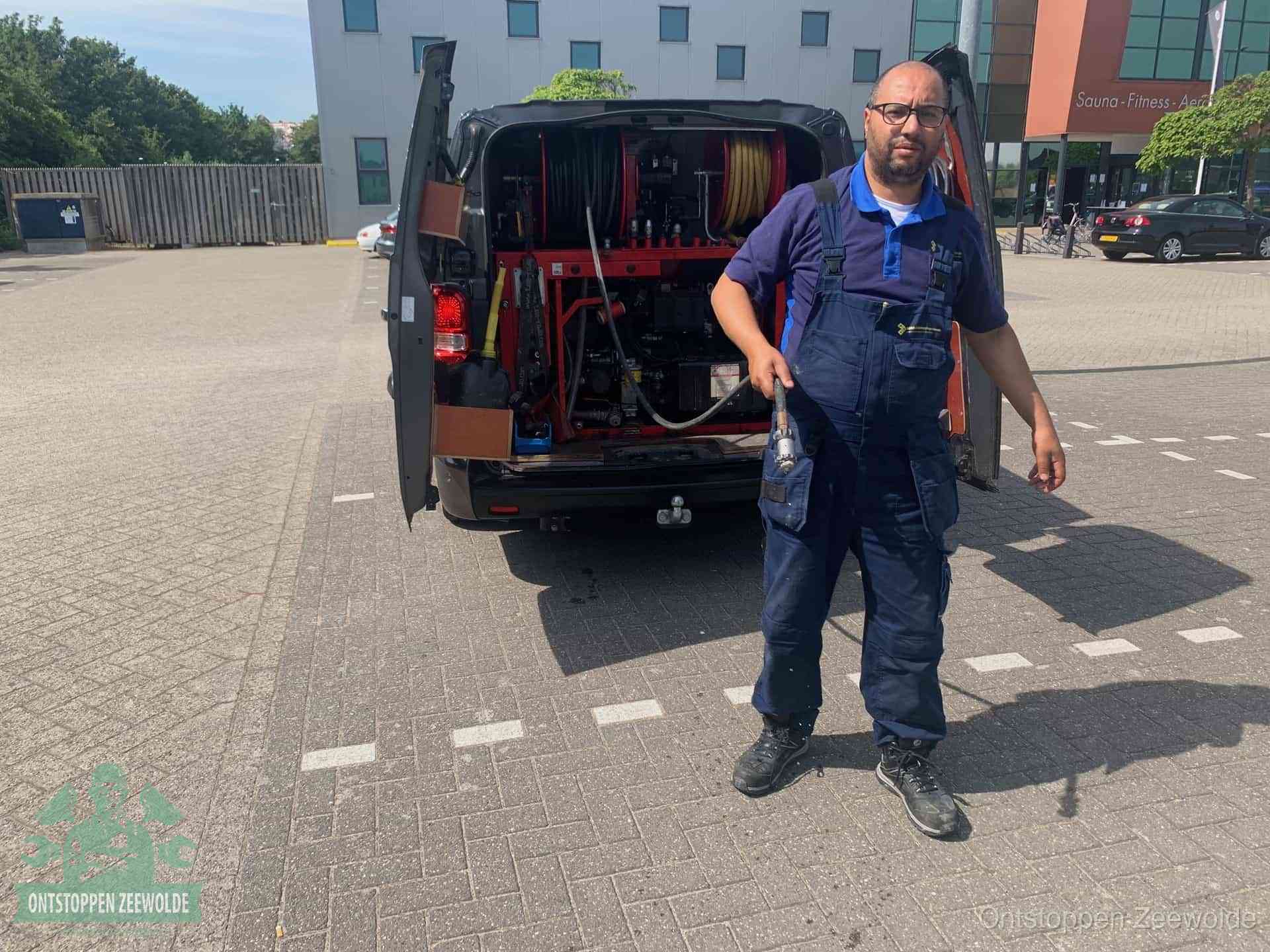 Een monteur bij zijn bestelbus met een hogedruk- en rioolreinigingsunit, klaar om de oorzaak van terugkerende wc-verstoppingen aan te pakken in Zeewolde