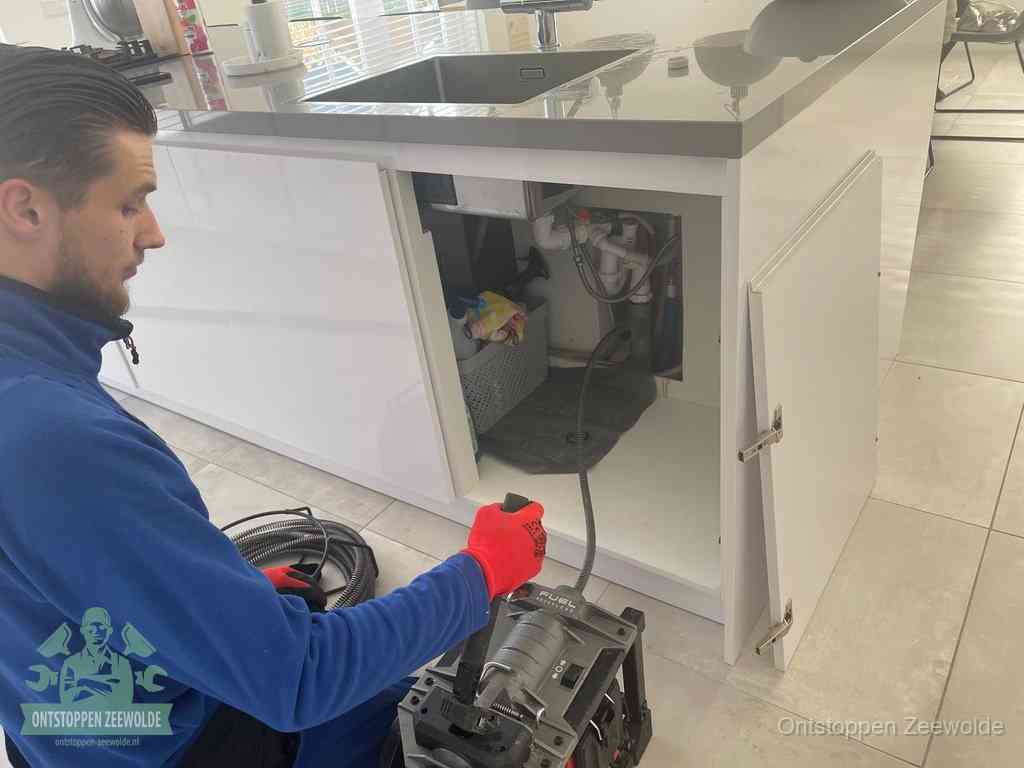 Monteur ontstopt met een veermachine een verstopte afvoer onder de gootsteen in Zeewolde