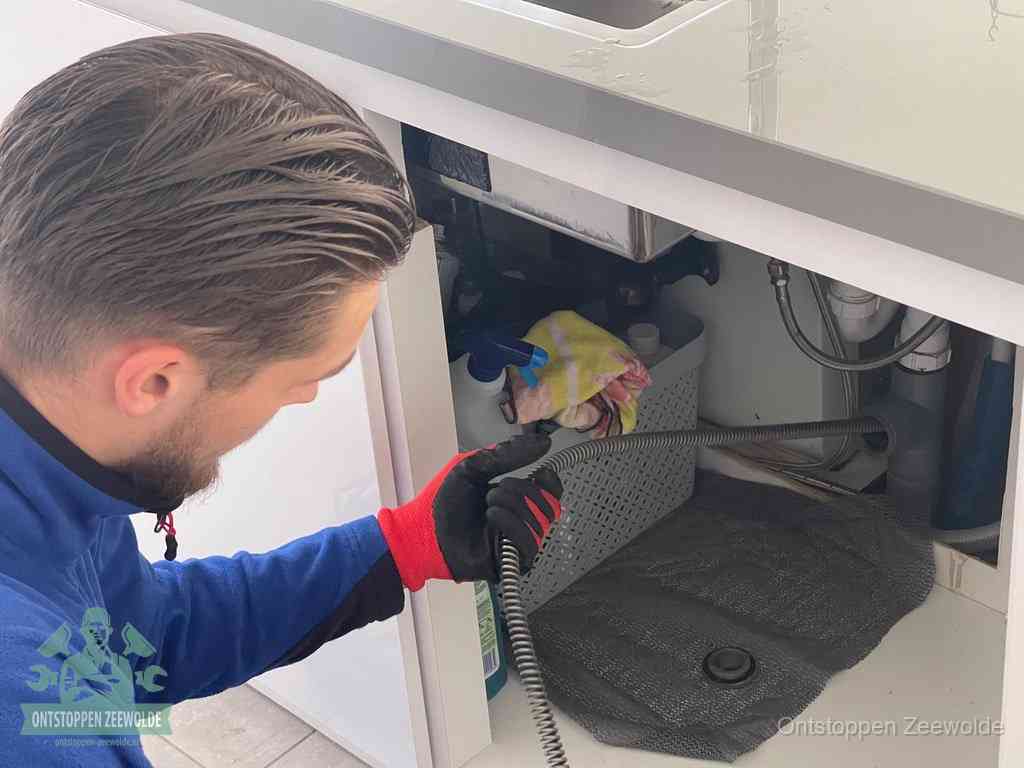 Een monteur voert een flexibele ontstoppingsveer in de afvoer om een verstopping voorbij de bocht van het toilet te bereiken in Zeewolde