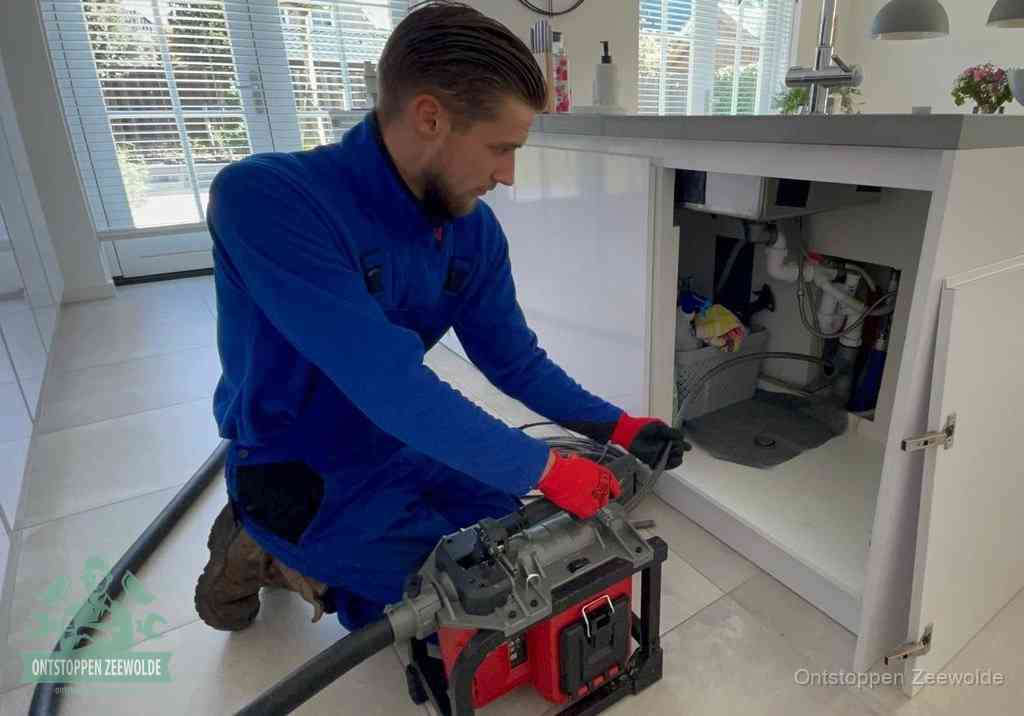 Een monteur voert een professionele elektrische ontstoppingsmachine in de afvoer onder de spoelbak tijdens het gootsteen ontstoppen in Zeewolde